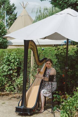 harriet playing the harp outside at a wedding drinks reception in cambridgeshire