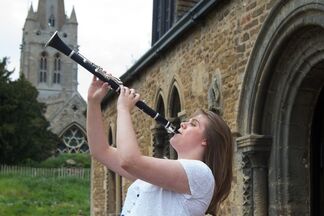 woman in white top playing clarinet with church in background